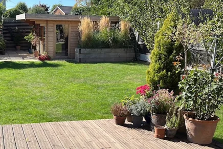 Wooden cabin set in a well-designed landscape with lush plants and green lawn.