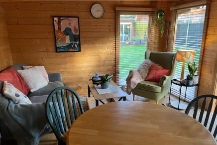 Inviting cabin room with natural wood finishes, a blue chair, round table, bookshelf, couch and armchair.