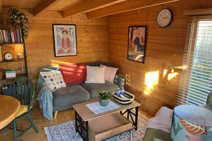 Inviting cabin room with natural wood finishes, a blue chair, round table, bookshelf, and couch