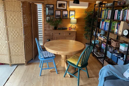 Inviting cabin room with natural wood finishes, a blue chair, round table, bookshelf, and couch
